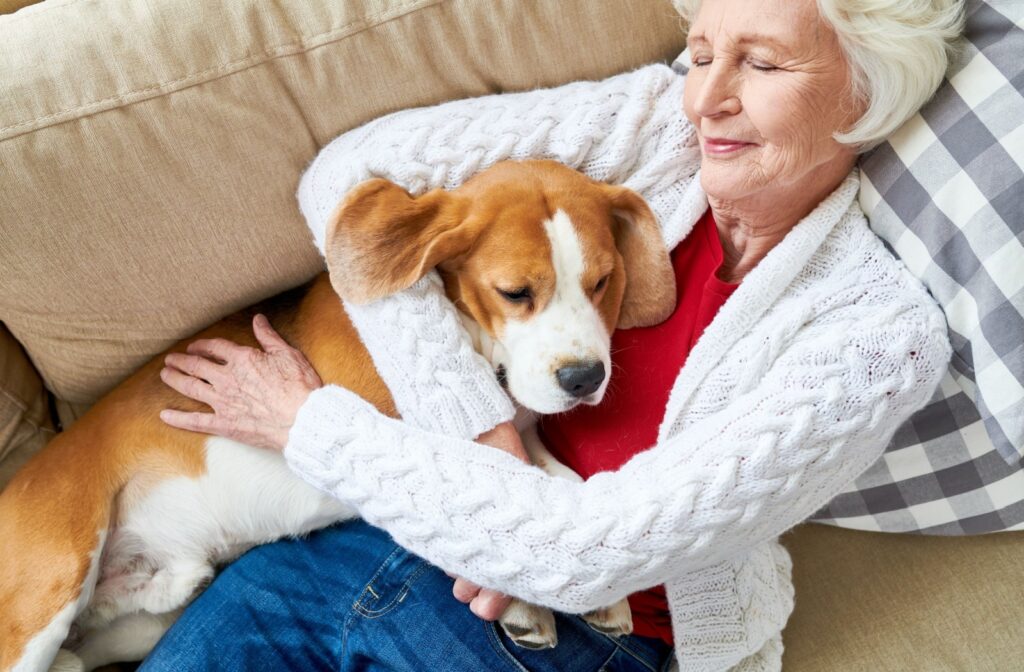 An elderly woman lying on a couch while gently hugging her pet dog.